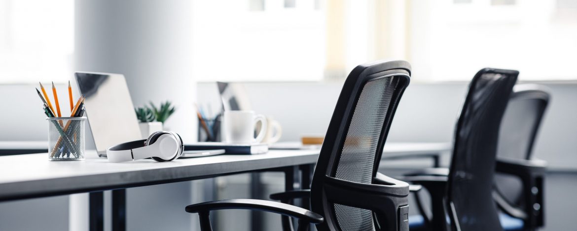 Modern gadgets in interior of coworking office during COVID-19 epidemic. Chairs and desk for support workers, laptops and headphones, cups and stationery in daylight on window background, free space