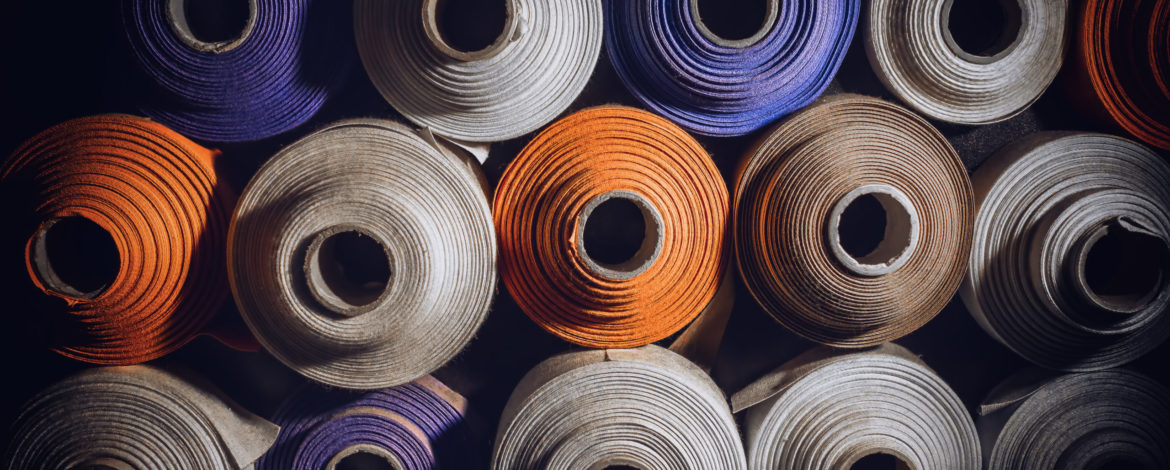 many textile rolls of blue, white and orange colors stacked one over the other in dark light