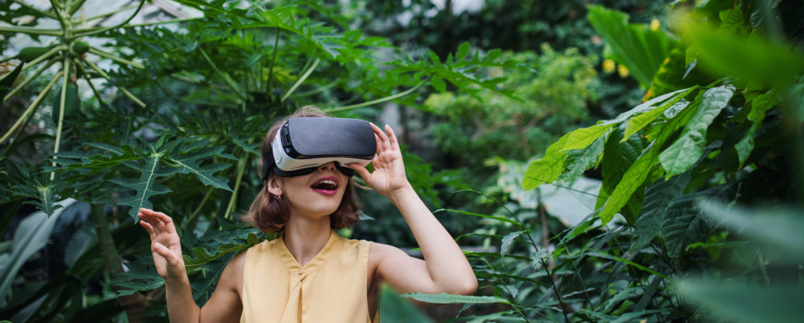 A front view of young woman standing in botanical garden, using VR glasses.