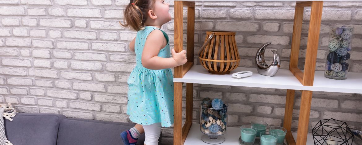 Cute Toddler Girl Standing On Sofa And Reaching For Toys On Shelf
