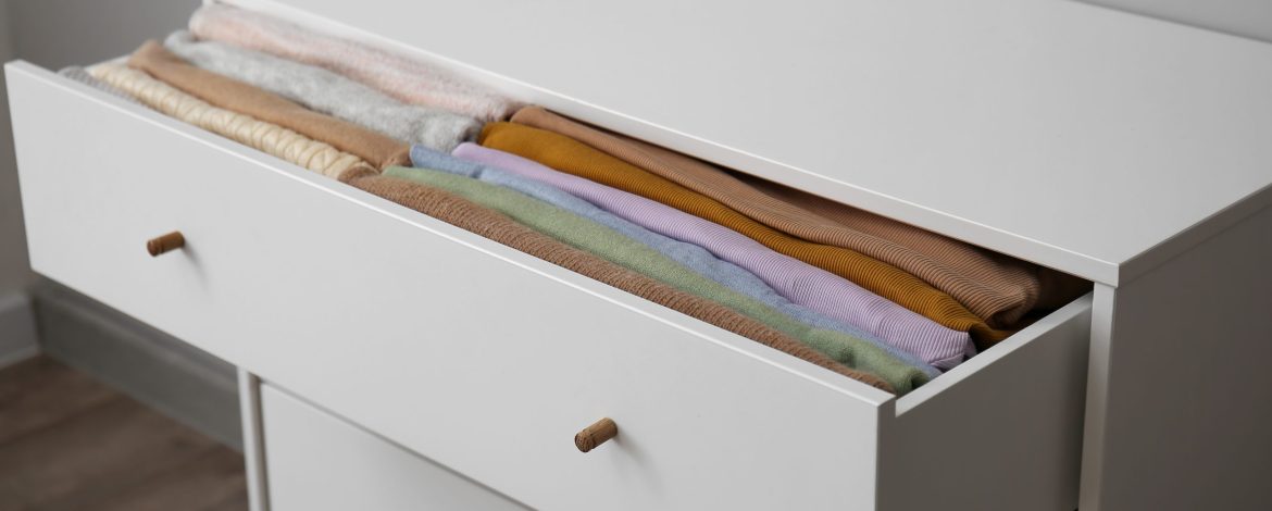 Open drawer with folded clothes in room, closeup